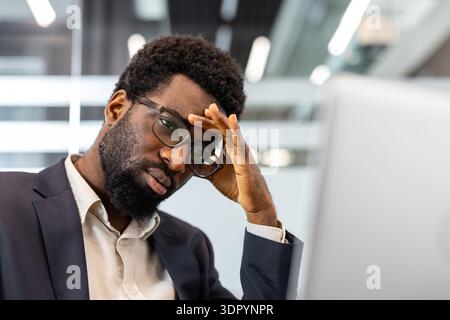 Uomo d'affari concentrato che soffre stress e frustrazione mentre lavora su un computer in ufficio, affrontando pressione, sovraccarico, fatica e pensiero intenso Foto Stock