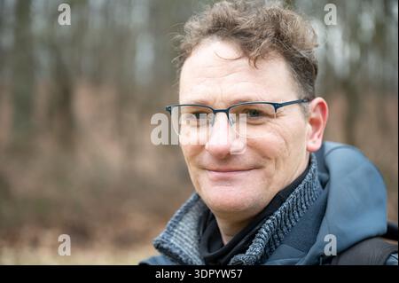 Ritratto della testa e delle spalle di un escursionista caucasico di 46 anni con capelli biondi scuri e occhiali, sfondo naturale. Lovanio, Belgio 14 FEB 2026 Pho Foto Stock