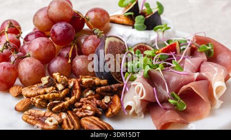 Tagliere di antipasti con carne, formaggio, uva, noci e fichi freschi. Primo piano vassoio in marmo per salumi. Foto Stock