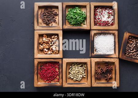Varietà di spezie ed erbe disposte in contenitori di legno su una superficie scura Foto Stock