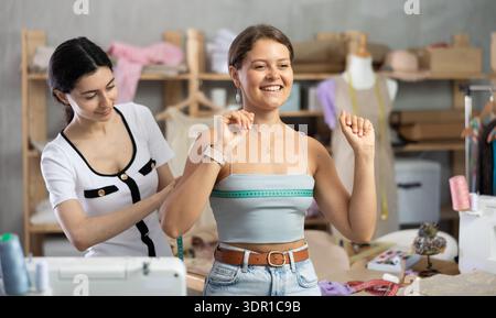 Sarta donna che effettua misurazioni da una cliente donna in officina Foto Stock