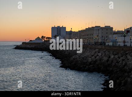 Vista al crepuscolo del lungomare di Cádiz con la banchina, gli edifici della città e i semafori lungo la costa di Cádiz, Andalusia, Spagna. Foto Stock