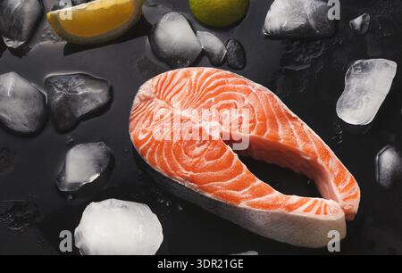 Filetto di salmone fresco con ghiaccio e agrumi su sfondo nero pronto per cucinare e servire Foto Stock
