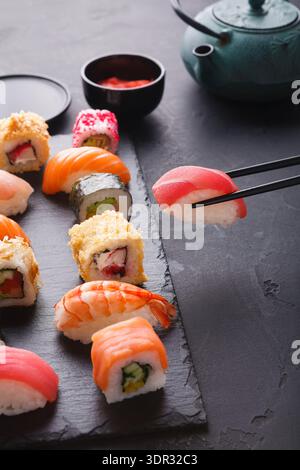 Collezione di sushi su un piatto nero con bastoncini e teiera in un ambiente da pranzo Foto Stock