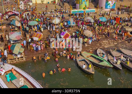 La vista aerea di una vivace scena si dispiega con le barche che costeggiano i ghati mentre la gente si riunisce per i rituali lungo il fiume Gange, Varanasi, Uttar Pradesh, Indi Foto Stock
