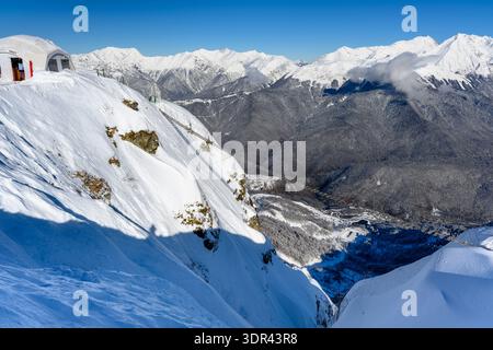 Un ponte sospeso su un precipizio, un'attrazione estrema. Una pittoresca catena montuosa innevata si innalza maestosamente contro un cielo azzurro. Foto Stock