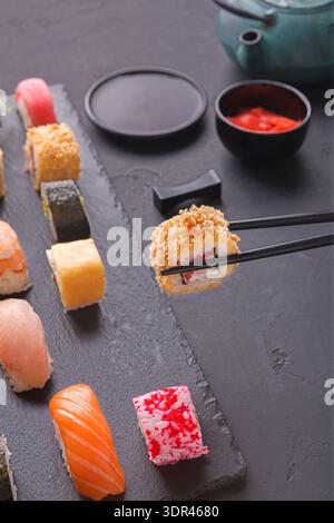 Collezione di sushi su un piatto nero con bastoncini e salse in un ambiente informale Foto Stock