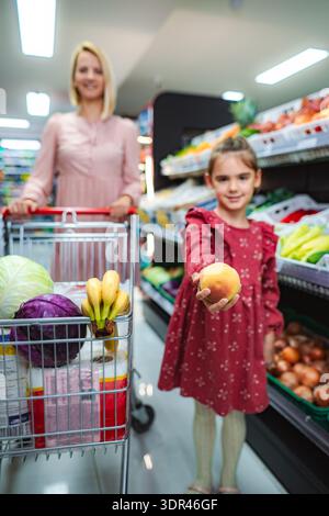 Figlia che tiene la pesca mentre la madre spinge il carrello della spesa al supermercato Foto Stock