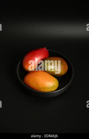 Mango biologico fresco in una ciotola di vetro su sfondo scuro Foto Stock