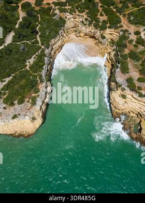 Vista aerea della spiaggia isolata incorniciata da aspre scogliere dove il mare turchese incontra la sabbia dorata, Praia da Morena, Portogallo. Foto Stock