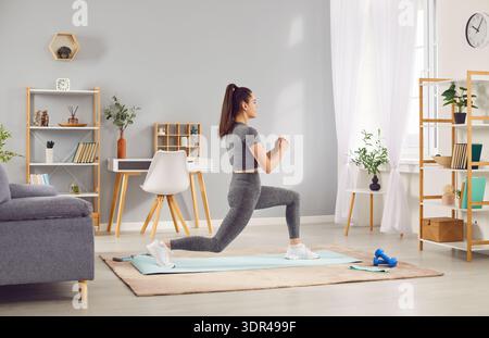 Donna attiva che fa affondi nella palestra Home Foto Stock