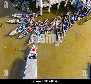 Vista aerea delle barche raggruppate sull'acqua, i loro colori vivaci contrastano con i toni terrosi dell'acqua e le strutture in legno ab Foto Stock