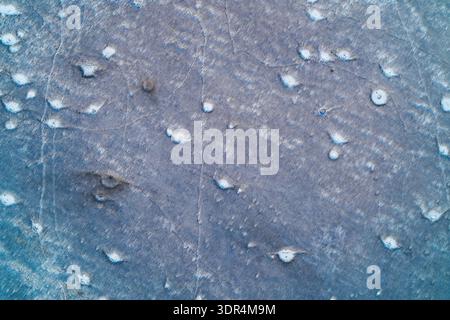 I crateri frastagliati di artiglieria feriscono la superficie ghiacciata di un campo invernale, creando un tragico schema astratto di guerra. Questa cupa vista aerea cattura l'impatto devastante del conflitto sul paesaggio Foto Stock