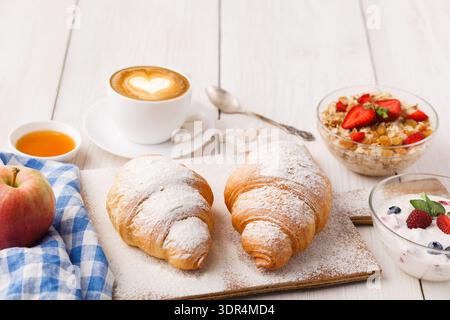 Raccolta di prodotti per la colazione con croissant, yogurt, frutta e caffè su un tavolo di legno Foto Stock