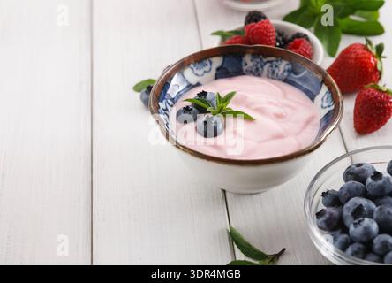 Preparazione di yogurt con frutta fresca in una ciotola su un tavolo di legno a casa Foto Stock