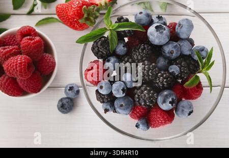 Collage di frutta con varie bacche organizzate in una ciotola e una piccola ciotola di lamponi Foto Stock