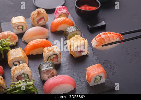 Collezione di pezzi di sushi con bastoncini su una superficie nera per un'esperienza culinaria Foto Stock