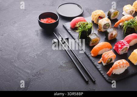 Collezione di sushi e panini disposti su un piatto nero con salse e bastoncini Foto Stock