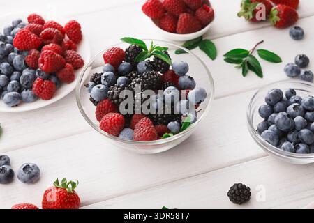 Bacche fresche disposte in ciotole su un tavolo di legno con foglie verdi Foto Stock