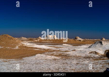 Ampia vista delle formazioni rocciose di gesso nel deserto bianco dell'Egitto vicino a Farafra, mostrando un vasto terreno arido, un cielo limpido e spettacolari forme geologiche adatte Foto Stock
