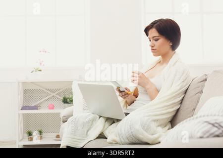 Una donna siede su un divano con un laptop aperto davanti a sé Foto Stock