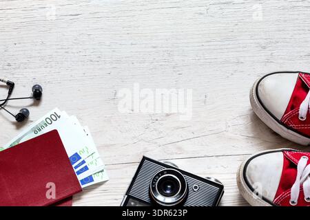 Accessori da viaggio con scarpe da ginnastica rosse, fotocamera retrò e altri oggetti su un tavolo in legno bianco con spazio per copiare. Concetto di viaggio. Foto Stock