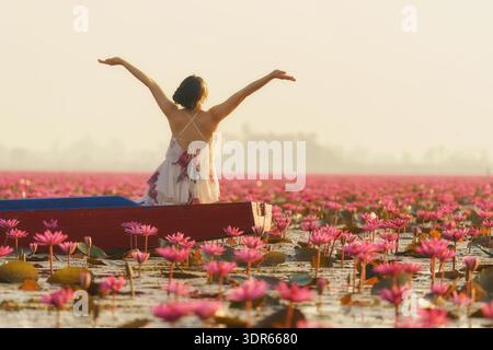Vista posteriore di una giovane donna con le braccia allungate seduta su una barca, Red Lotus Sea (Talay Bua Daeng), Udon Thani, Thailandia nord-orientale Foto Stock