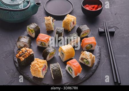 Diversi tipi di sushi sono collocati in un cerchio su una scura tavola di ardesia Foto Stock