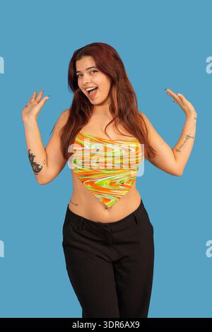 Giovane donna con i capelli rossi che indossa un colorato top e pantaloni neri su sfondo blu Foto Stock