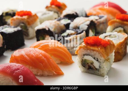 Varietà di Sushi Rolls e Sashimi serviti su un piatto bianco in un ambiente informale Foto Stock