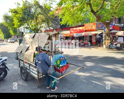 Donna con un bambino, raccolta rifiuti o riciclatore informale a Phnom Penh, Cambogia, seduta su un carrello pesante Foto Stock