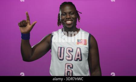 La maglia da basket Man in usa mostra i pollici e la mano alzata in studio con sfondo magenta; celebrazione della fiducia. Foto Stock