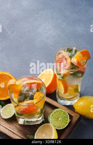 Bevande rinfrescanti alla frutta con agrumi e ghiaccio su un vassoio di legno in un ambiente da cucina Foto Stock