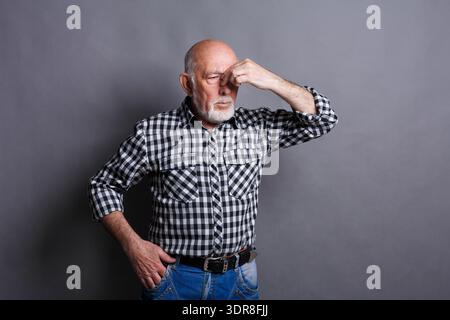 Uomo con camicia a scacchi in piedi con la mano sulla fronte davanti a sfondo grigio Foto Stock