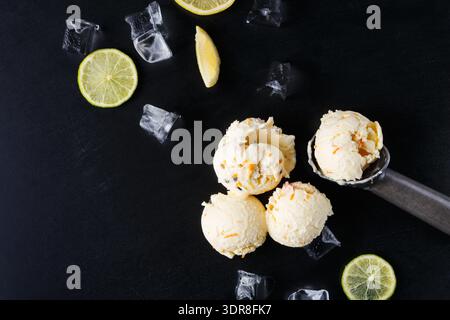 Cucchiai per gelato con fette di limone e cubetti di ghiaccio su una superficie scura in un ambiente di cucina Foto Stock