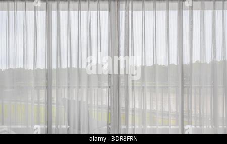 Interno di un soggiorno vuoto con grande finestra luminosa e tende bianche Foto Stock