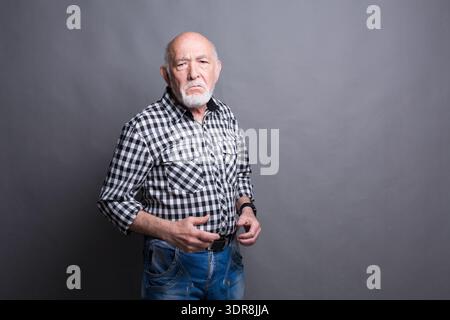 Uomo con una camicia a scacchi si staglia su uno sfondo grigio in un locale interno Foto Stock
