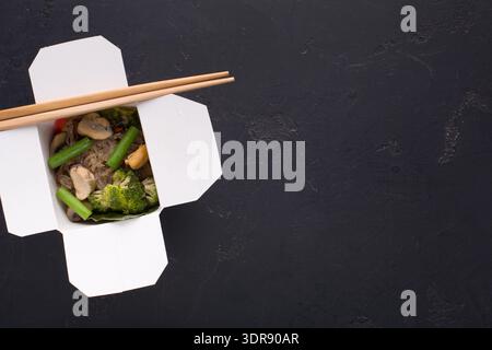Raccolta di cibo in una scatola da asporto con bastoncini su una superficie scura Foto Stock
