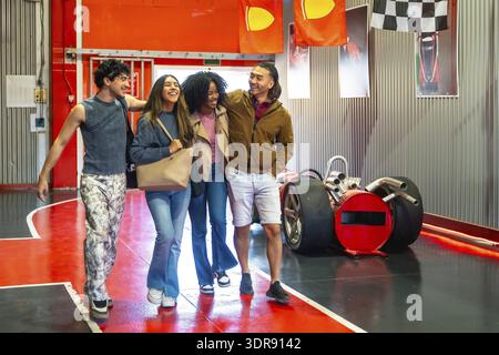 Gruppo di quattro diversi giovani amici adulti che camminano insieme e ridono, trovano la felicità e si divertono a divertirsi all'interno di un animatore al coperto Foto Stock