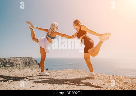 Yoga donne scogliera che eseguono esercizi di equilibrio su una cresta panoramica che si affaccia sull'oceano durante una giornata di sole Foto Stock
