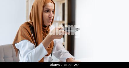 Medico donna musulmana in hijab che utilizza lo smartphone per il riconoscimento vocale ai in ospedale o in clinica. Foto Stock