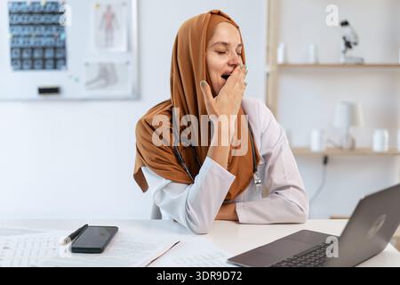 Medico generico arabo professionista. Stanco medico musulmano in hijab ha sorpreso coprendo la bocca mostrando sonnolenti sbadigliate lavoravano troppo Foto Stock