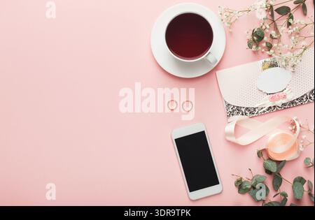 Collezione di oggetti disposti su una superficie rosa con tè, fiori e anelli Foto Stock