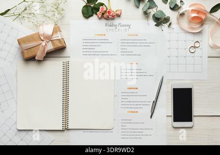 Raccolta di articoli per la pianificazione di matrimoni su un tavolo con elenco di controllo, notebook e decorazioni Foto Stock