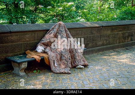 Eingescanntes Diorgov einer historischen Farbaufnahme eines unter einer Decke sitzenden, totale verhüllten Obdachlosen auf einer Parkbank im Central Foto Stock