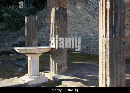 Pompei, Italia, antiche colonne romane e bacino in pietra presso il sito archeologico in una giornata di sole. Foto Stock