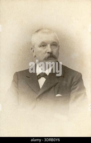 Questo ritratto di studio ravvicinato del 1897-1912 di Adriaan Boer mostra un olandese più anziano con i baffi. Indossa un choker e una giacca con un fazzoletto tascabile. La fotografia è una carte de visite, che mette in evidenza l'espressione facciale, l'abbigliamento, la postura e la composizione tipica della fotografia da studio olandese di Baarn del tardo XIX secolo e dell'inizio del XX secolo. Foto Stock