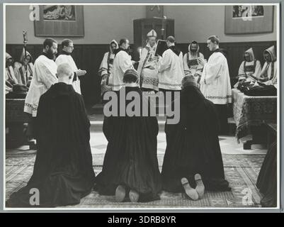 Una fotografia del 1938 documenta i monaci dell'abbazia benedettina di St. Andries vicino a Bruges che si inginocchiano durante la cerimonia di presa dei voti, ascoltando attentamente l'abate che impartisce ammonimenti dal suo trono. L'immagine illustra la disciplina monastica, l'osservanza rituale, la gerarchia liturgica, la pratica cattolica, la tradizione benedettina, vita comune e documentazione visiva storica. Foto Stock
