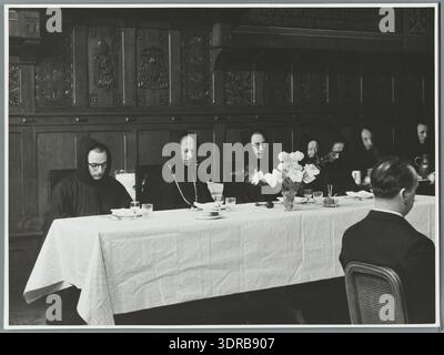 Una fotografia del 1938 dell'abbazia benedettina di St. Andries vicino a Bruges raffigura monaci che indossano cappe identiche seduti su un tavolo coperto dopo aver preso i voti. I monaci appena professati siedono al tavolo dell'abate, ascoltando una lettura prima del pasto. L'immagine documenta la cena monastica, la pratica cerimoniale, la tradizione benedettina, l'osservanza post-voto, la vita comunitaria cattolica, costumi liturgici e cultura monastica europea. Foto Stock