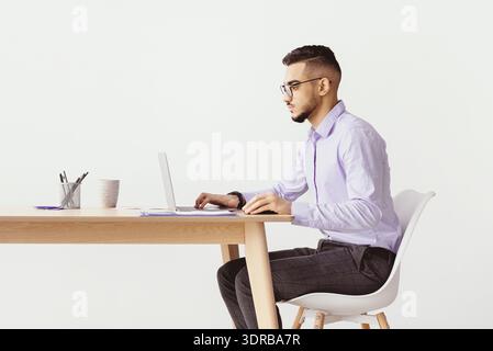 Giovane uomo che lavora su un laptop a una scrivania in una stanza luminosa durante il giorno Foto Stock